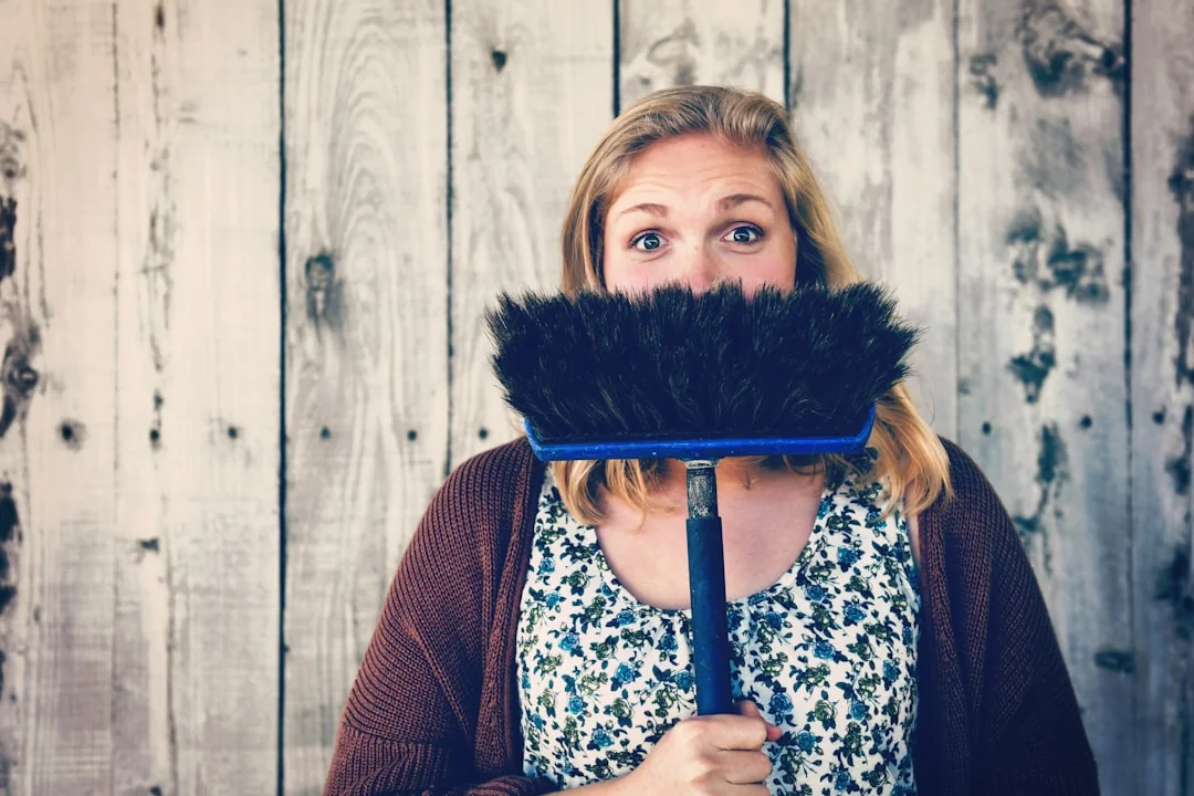 A hand using a feather duster to clean a wooden desk, surrounded by plants and office items.