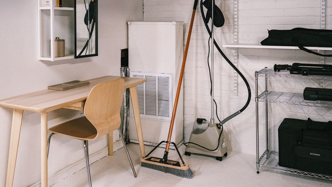 Un espace de bureau à domicile ordonné, avec un bureau en bois, une chaise, un balai et du matériel de nettoyage.